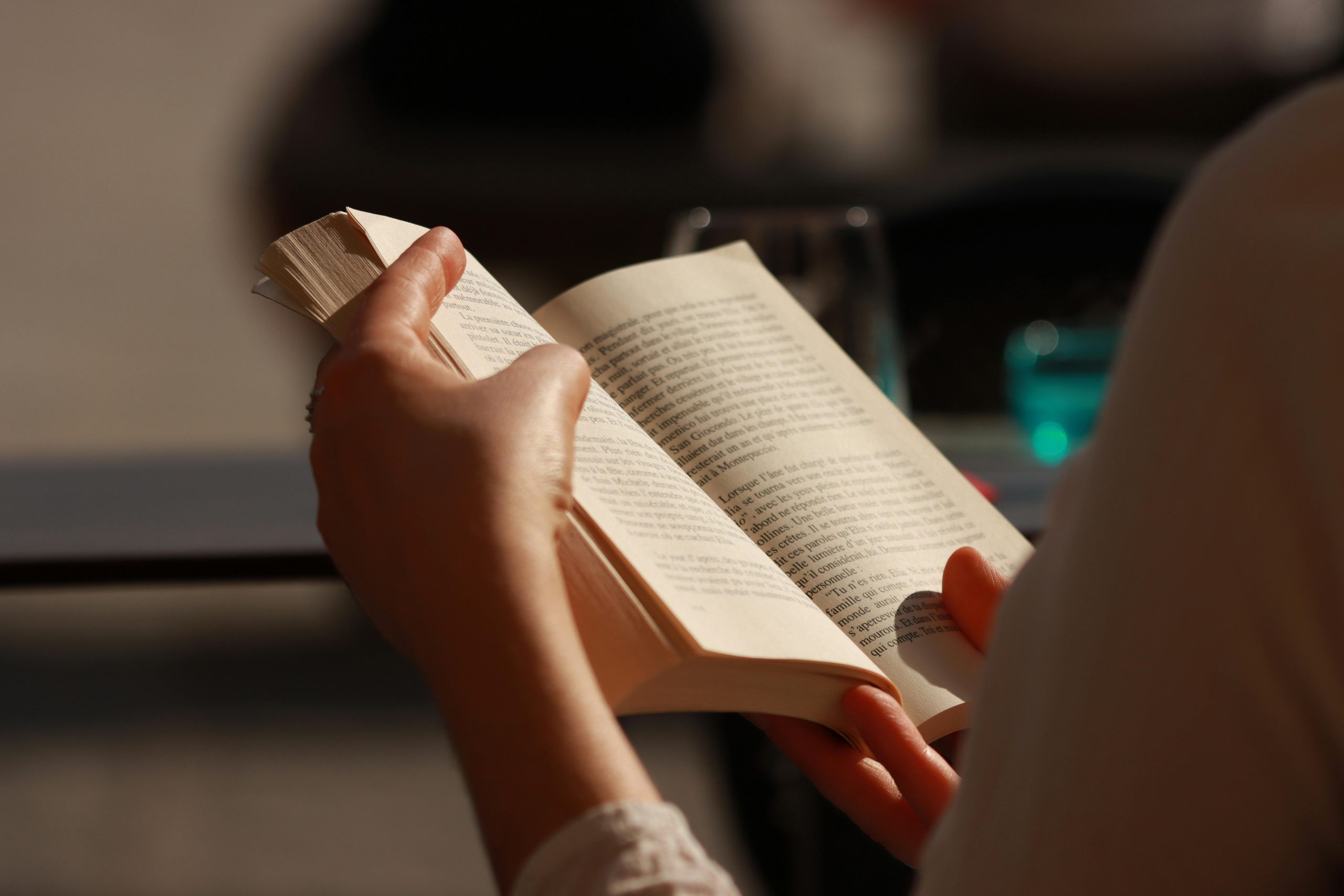 Close-up of hands holding and reading a book in warm natural light.