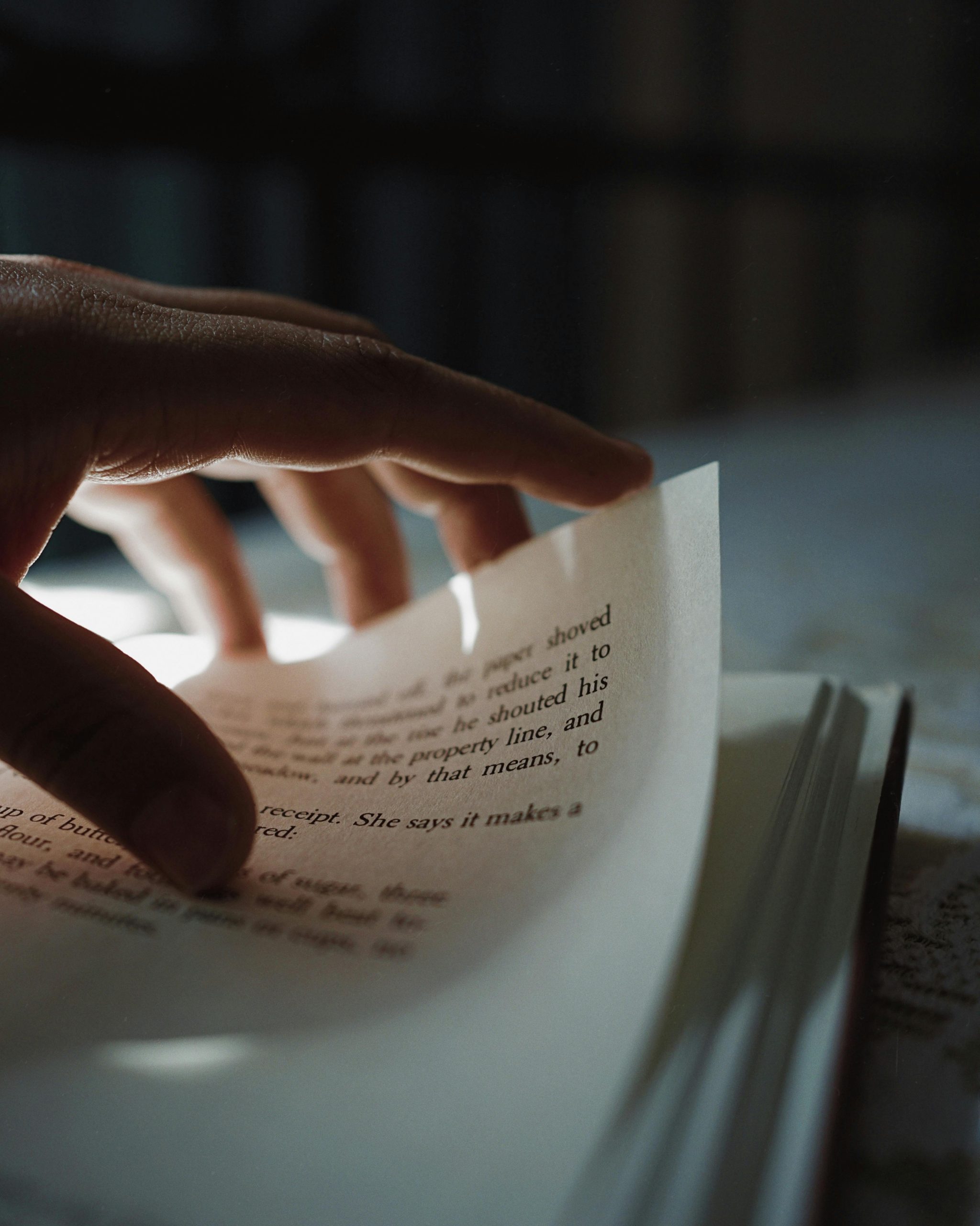 Close-up of a hand turning a page in an open book with blurry text in dim light.