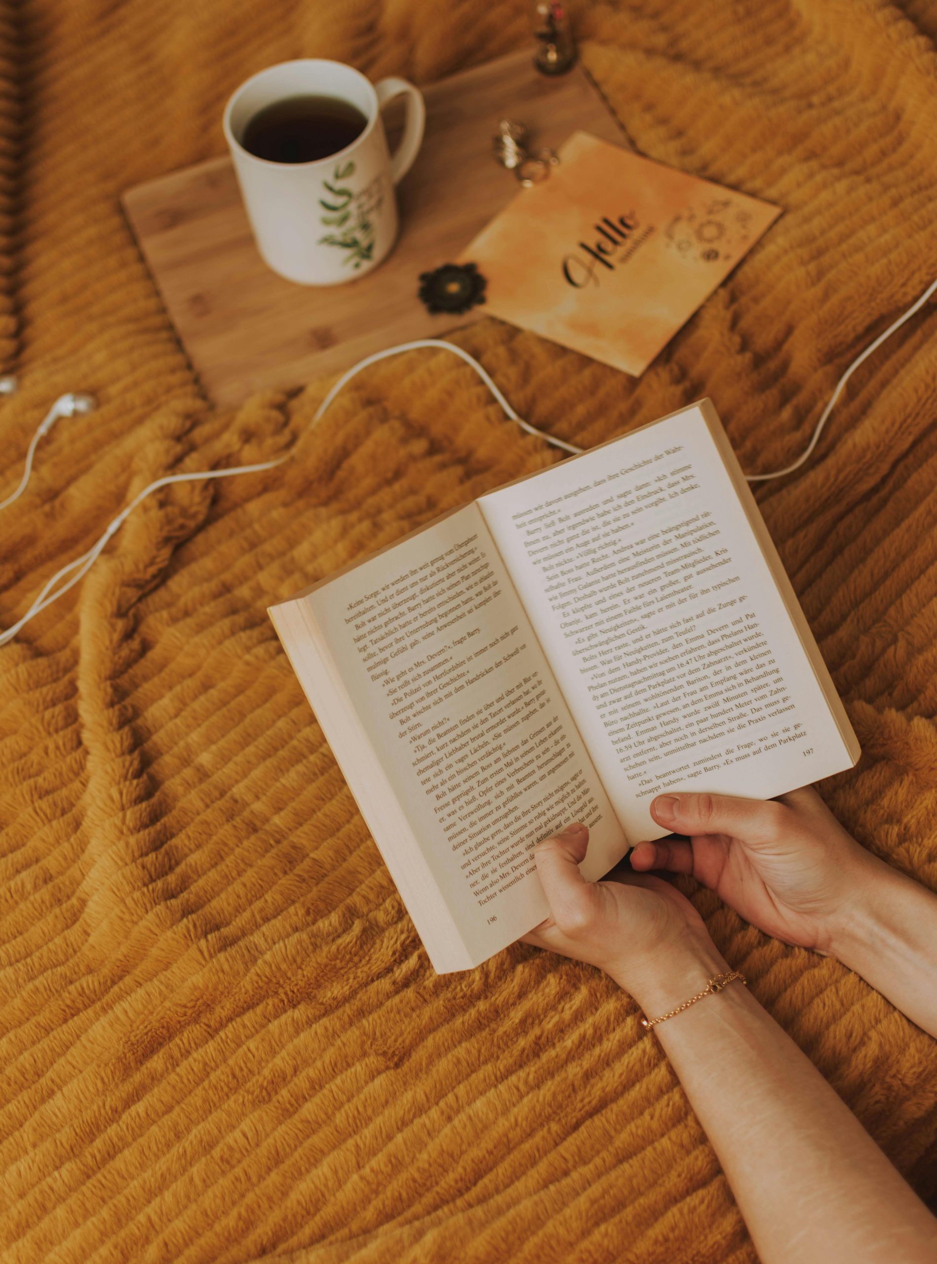 A person enjoying a relaxing reading session with a cup of coffee on a cozy bedspread.
